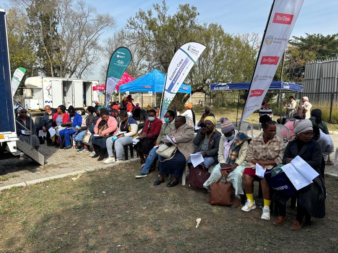 Community members seated outside a mobile clinic waiting for screening services at a SIOC-CDT outreach site